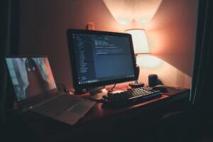Game developer working on code with two monitors in a dark room